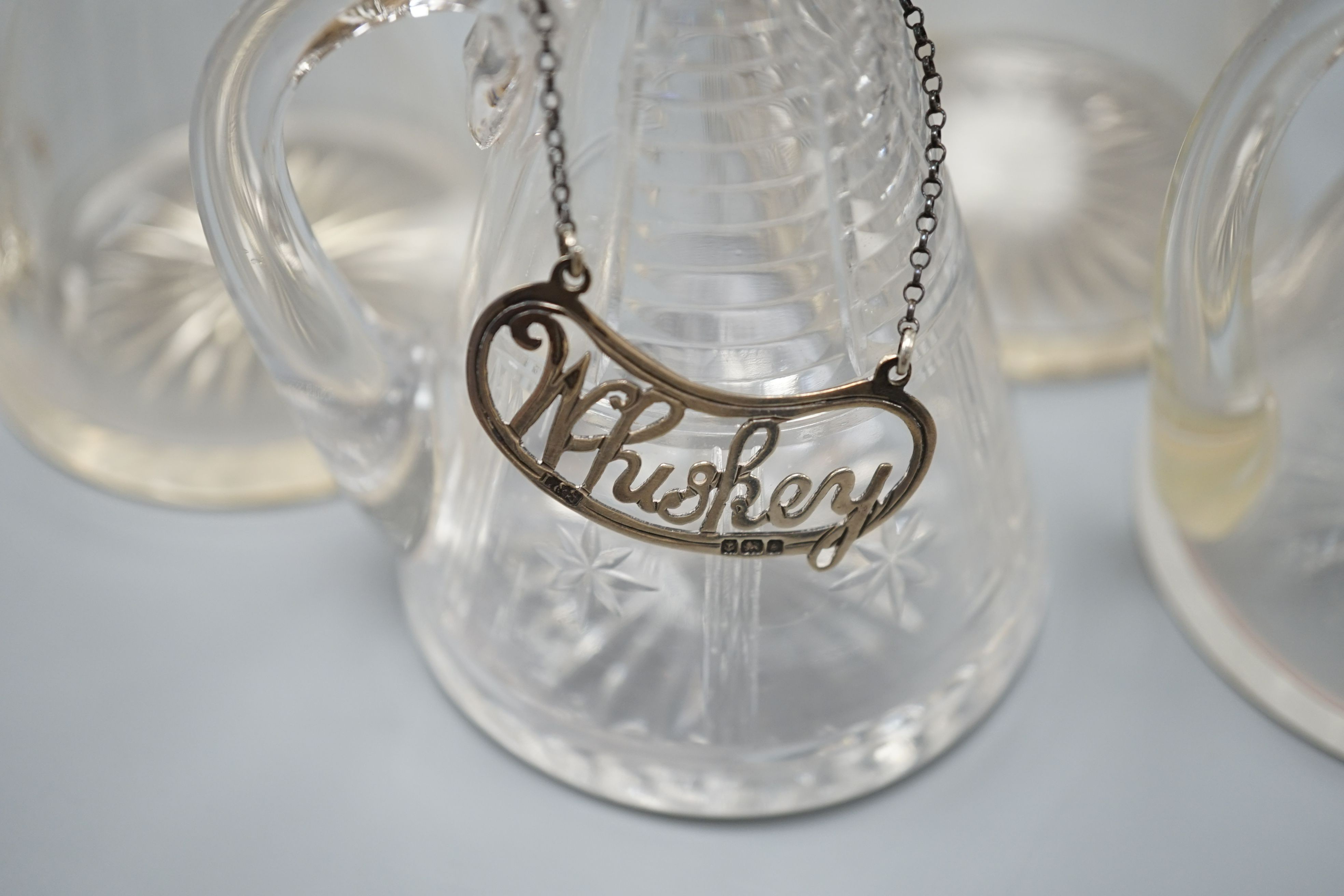 Five early 20th century and later silver mounted glass whisky tot jugs by Hukin & Heath, including a pair, Birmingham 1932, together with two silver Whiskey labels, 11cm.